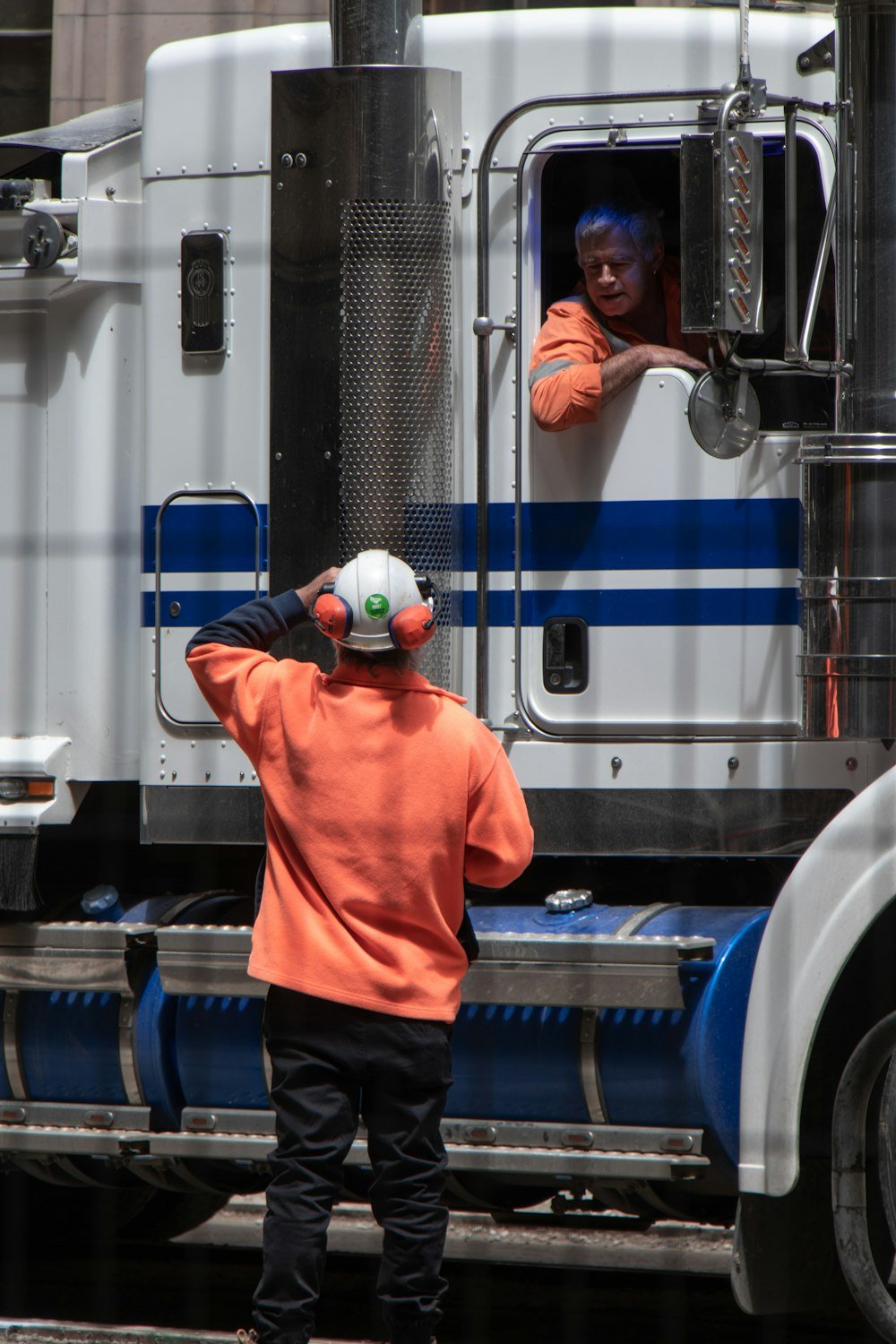 A man in a semi truck talking with a man standing on the ground